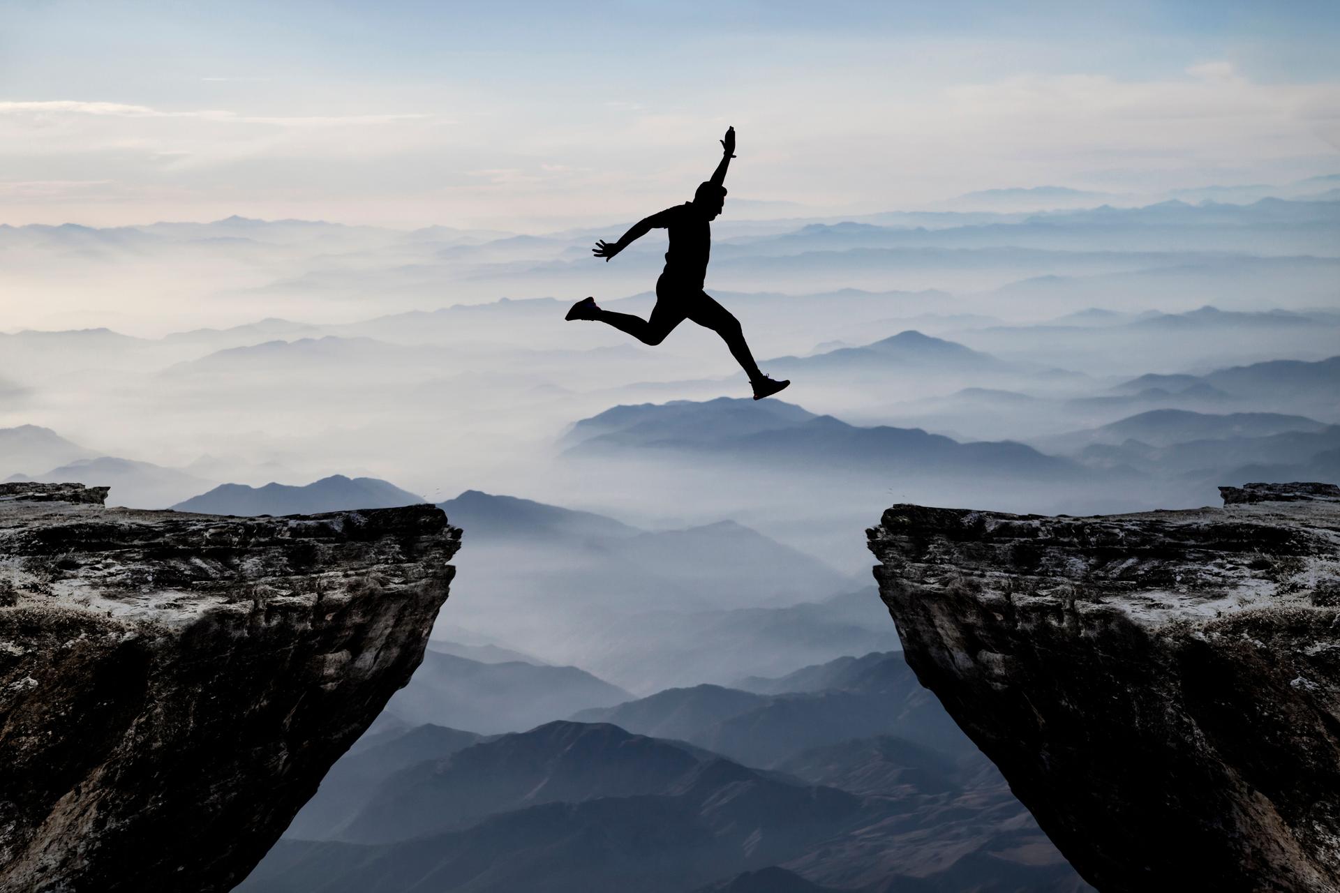 Silhouette of man jumping from one cliff to another cliff with excitement