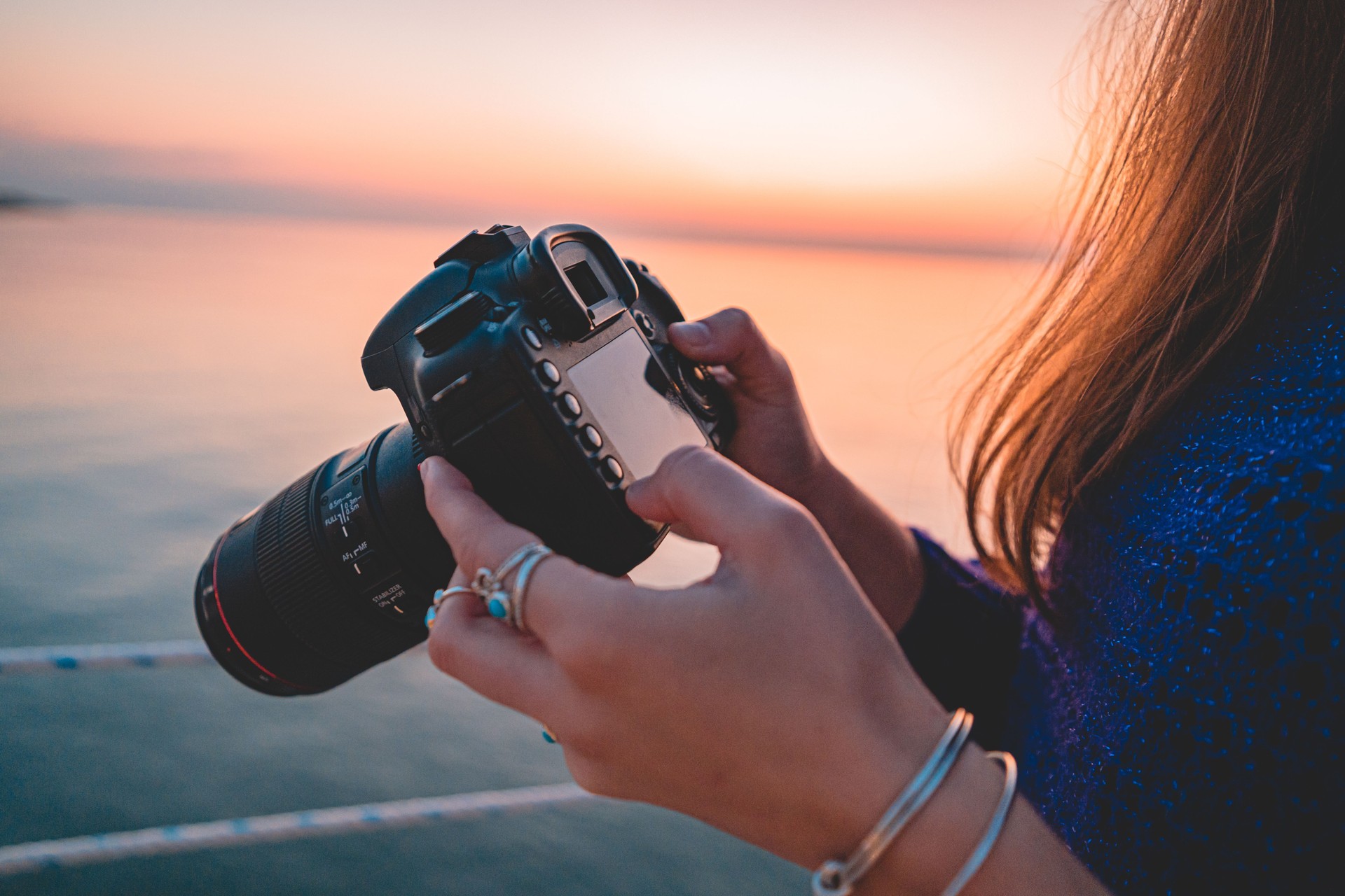 Woman photographer holds dslr camera during taking photos sea at sunset